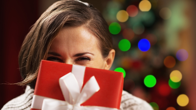 Happy young woman holding christmas present box in front of face
